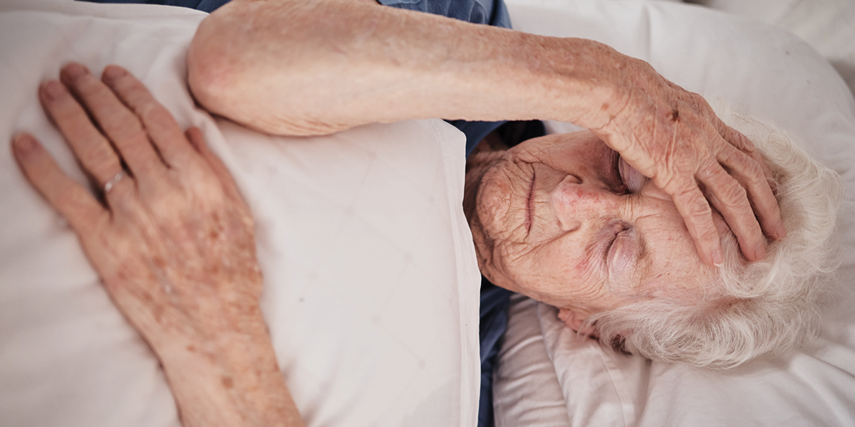 elderly woman laying prone covered with a blanket and hand on head