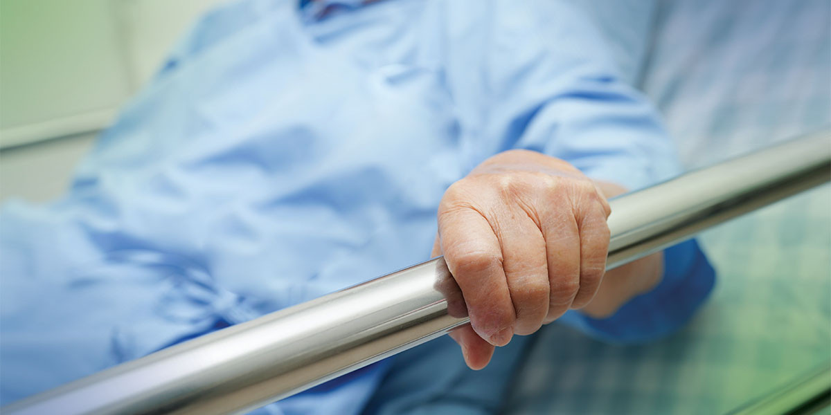person in hospital bed with hand on the rail