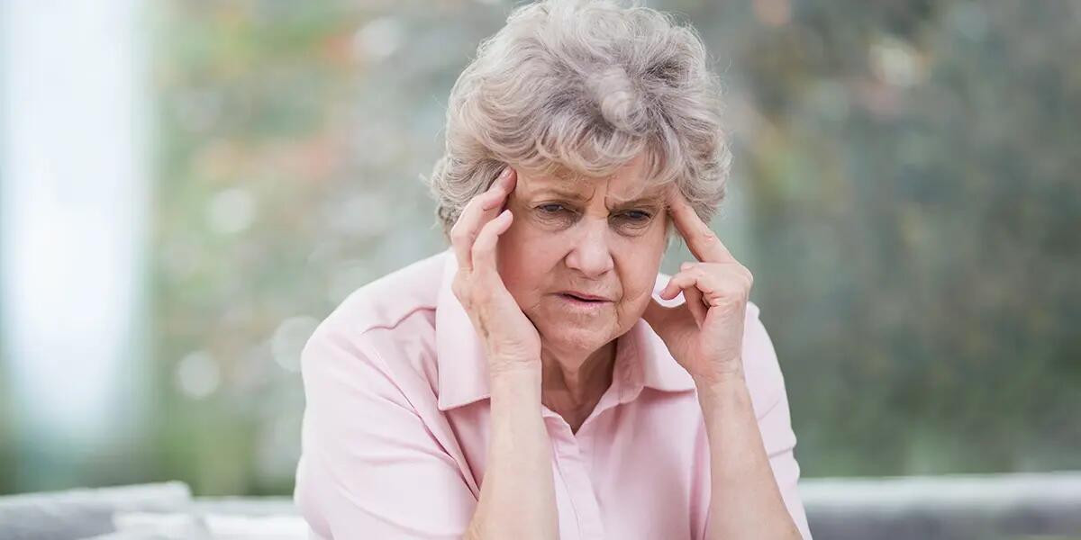 Elderly woman with fingers on temples, appearing confused