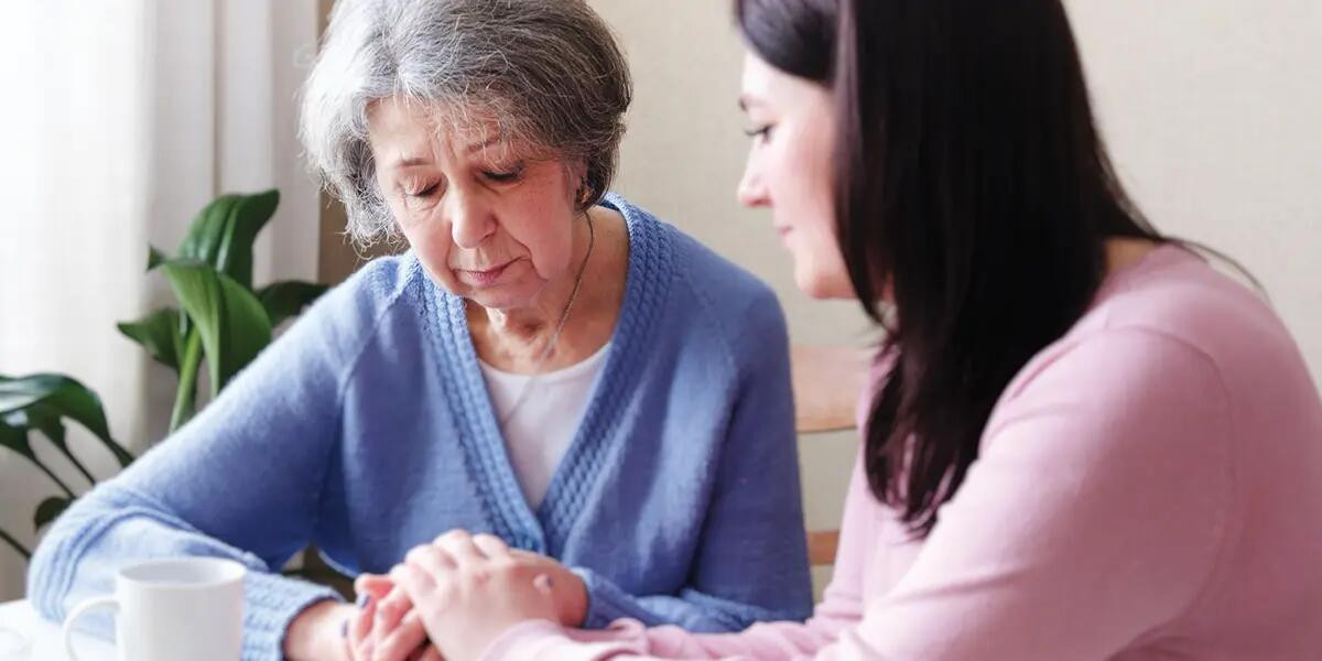elderly, solemn woman holding hands with younger woman