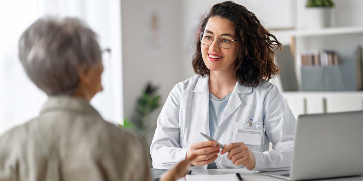 seated older adult at desk facing a smiling medical personnel