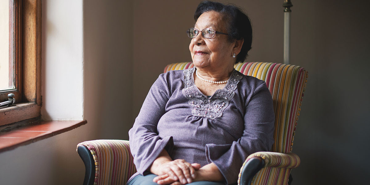 older adult woman seated in chair beside window looking outside happily