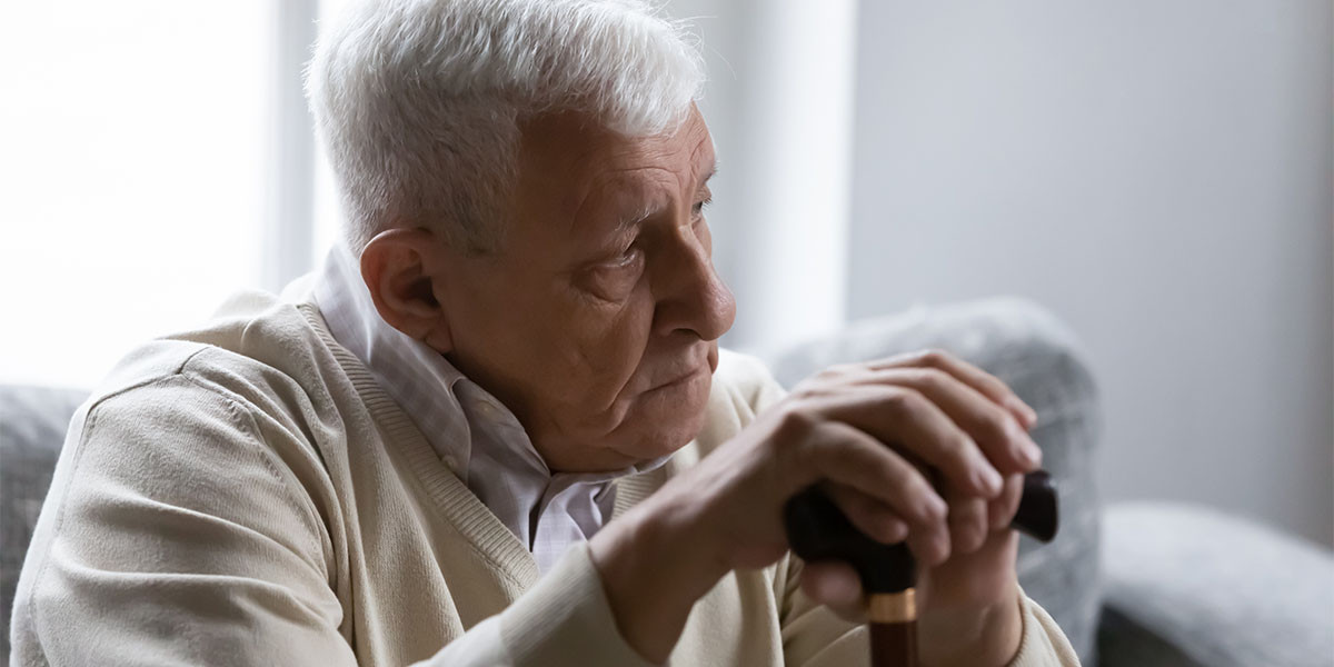 elderly man holding cane in both hands, looking concerned