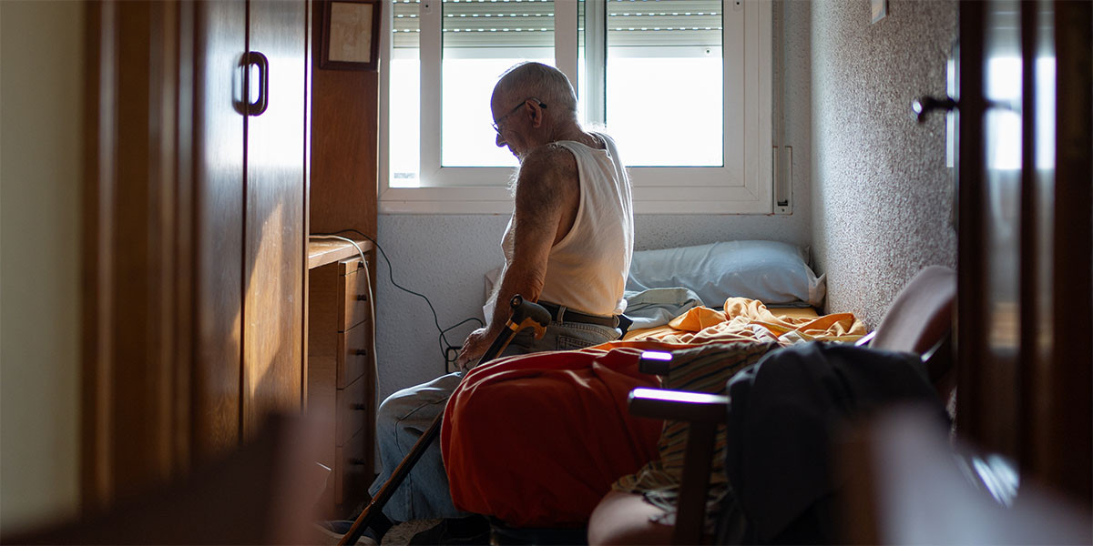 older adult man sitting on the site of the bed