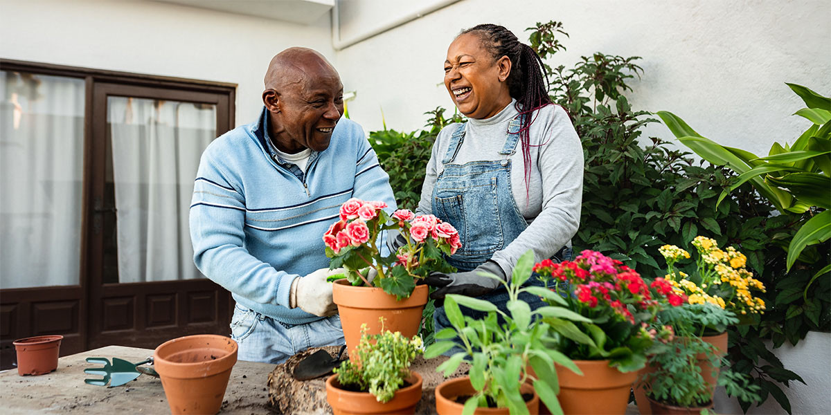 2 older adults smiling and planting flowers into terra cotta pots
