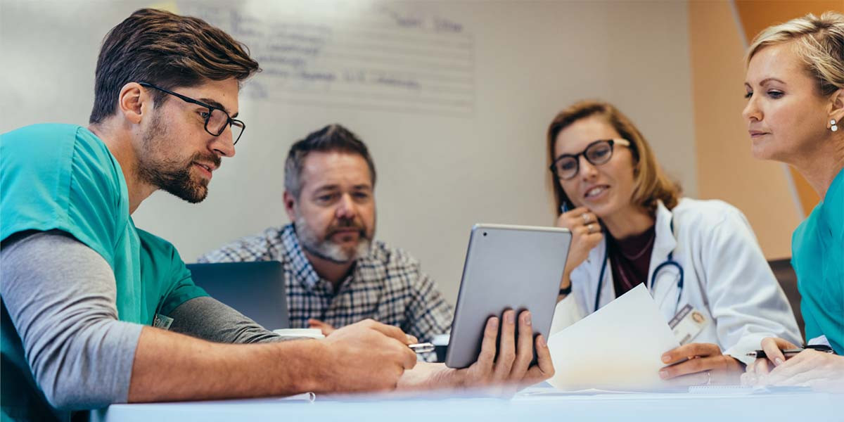 medical professionals gathered at conference table looking at a tablet