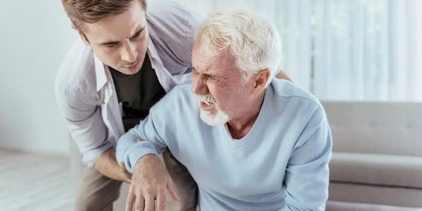 an elderly grimacing gentleman being helped by younger person