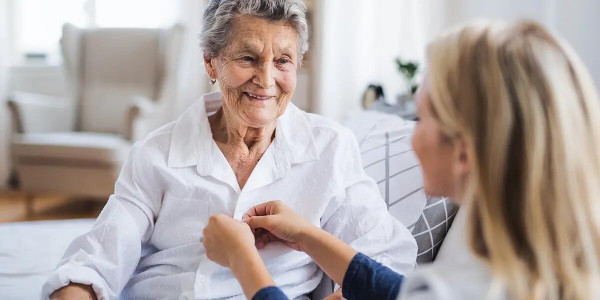 caregiver helping seated elderly woman with dressing