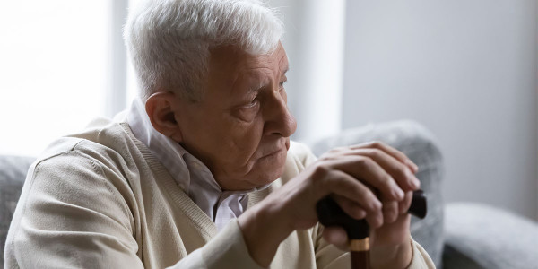 elderly man holding cane in both hands, looking concerned