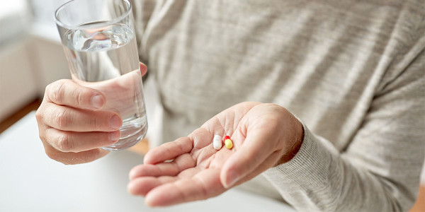 an elderly person's hands holding a glass of water and two pill medications