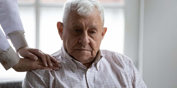 seated elderly gentleman with a pair of caregivher hands on his shoulders