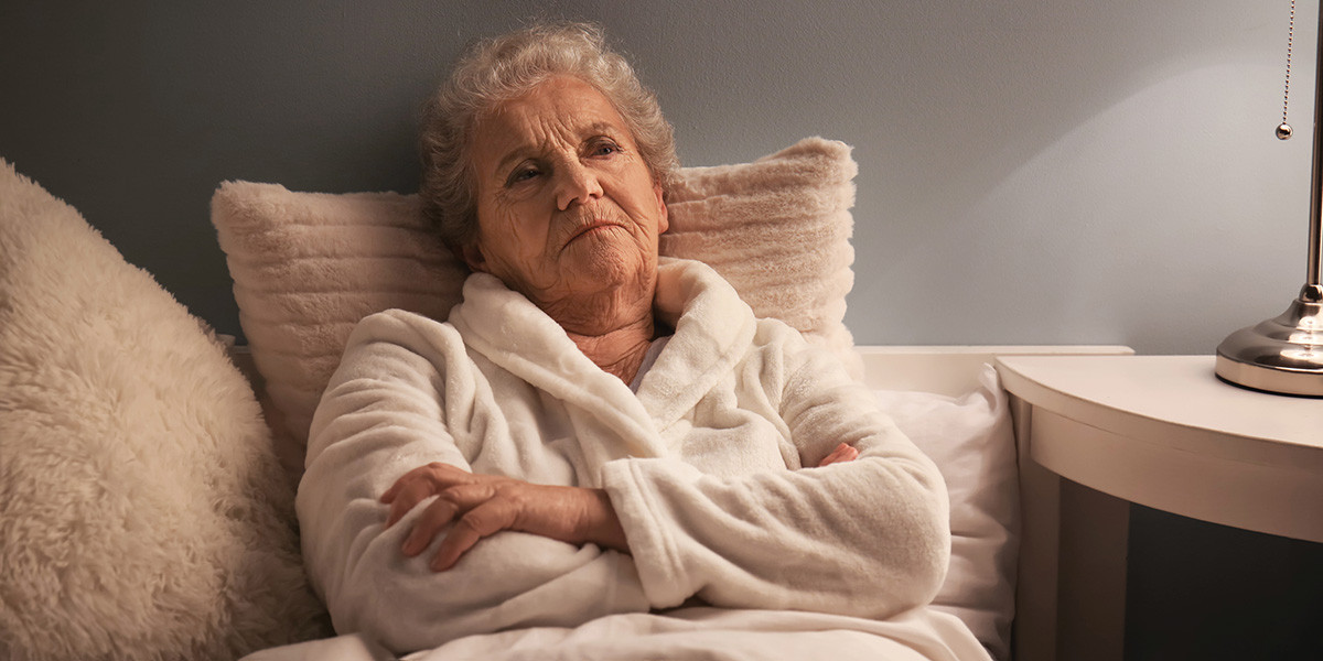 elderly woman wearing robe in bed with arms crossed and unhappy expression