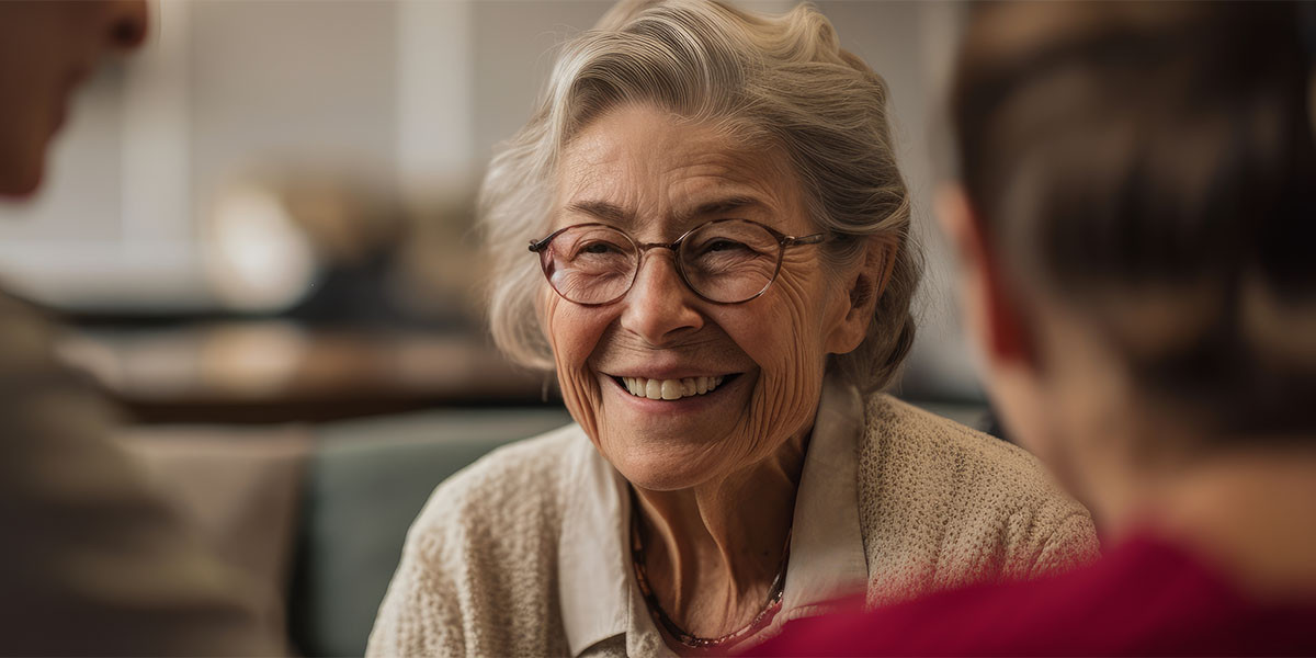 Smiling elderly woman with two other people out of focus facing her